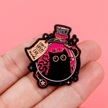 A hand holds KittyNook Cat Co.'s Black Cat Enamel Pin with wide eyes, top hat, and